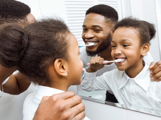 parent brushing their teeth with their child in the bathroom mirror